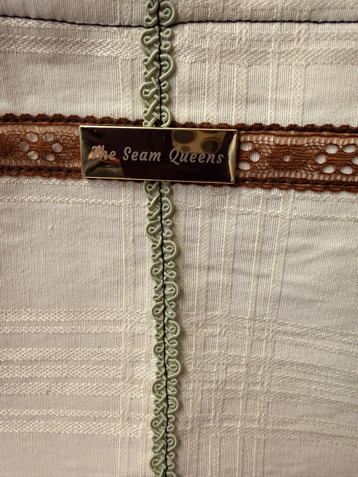 The Seam Queens gold label with brown lace and sage trim, close-up